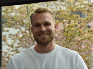 A muscleous chemistry student with a white T-Shirt standing in front of a blossoming cherry tree.